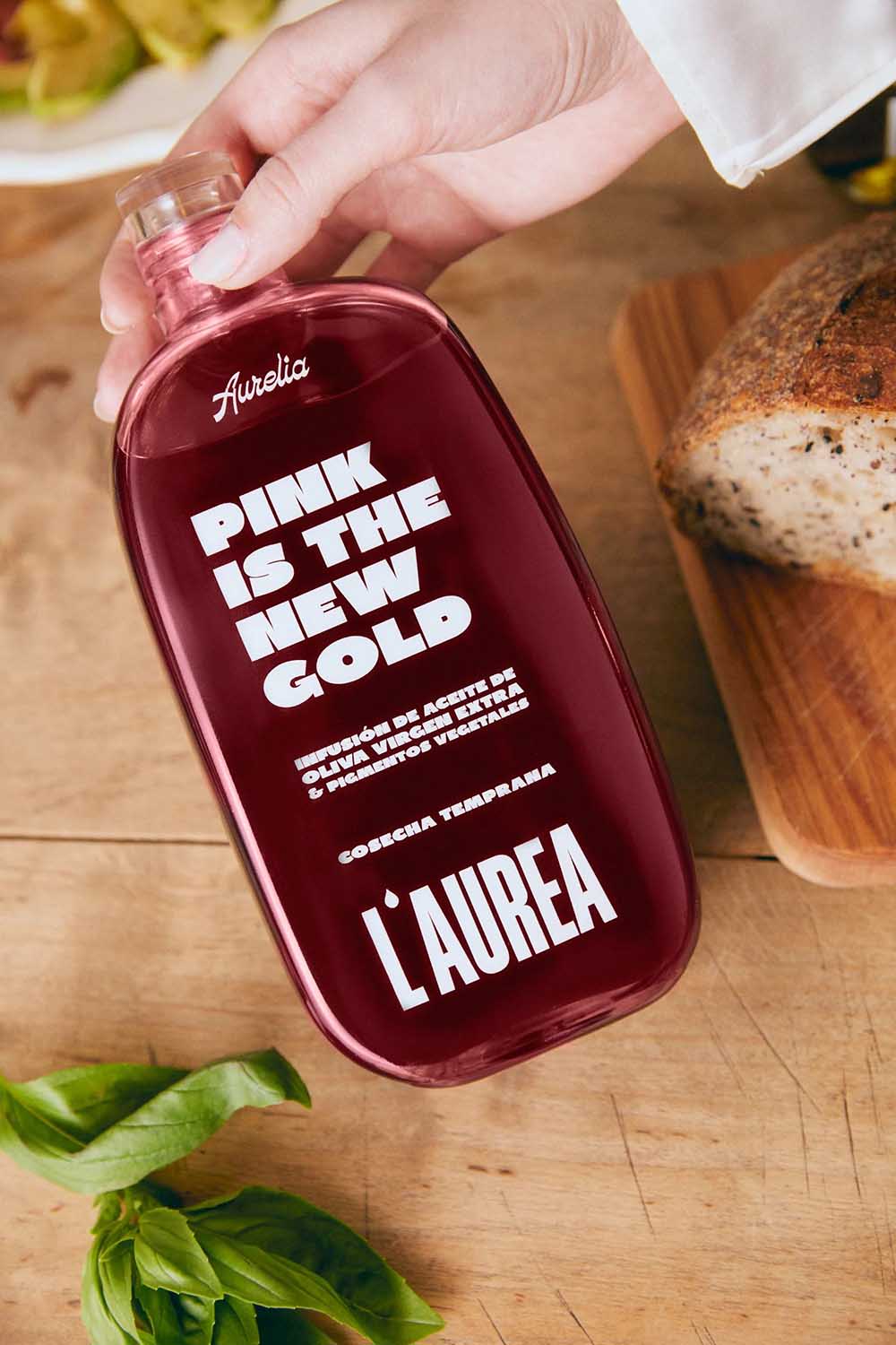 Botella rosa de L’AUREA para aceite de oliva con tipografía blanca de gran impacto
